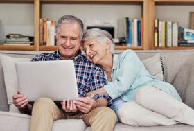 Una pareja feliz de séniors con un ordenador e Internet mayormente