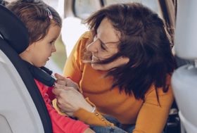 Madre sonriente ajusta el arnés de la silla del coche donde está sentada su hija