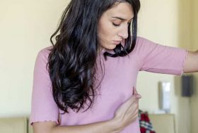 Erupción debajo del pecho, causas y tratamiento: mujer joven con camiseta rosa poniendo una mano debajo del pecho