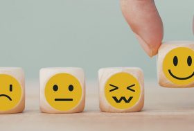 Ciclotimia: diferentes cubos de madera con emoticonos de diferentes estados de ánimo y una mano elige emoticonos de cara sonriente feliz