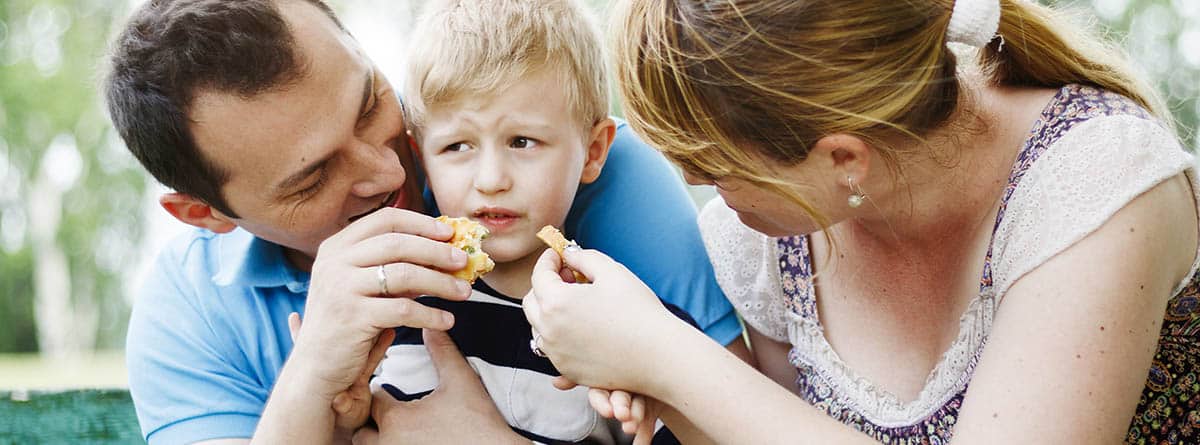 Madre y padre intentan alimentar a su hijo  en el parque que se niega a comer. 