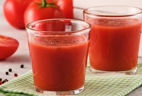 jugo de tomate en un vaso con tomates rojos maduros