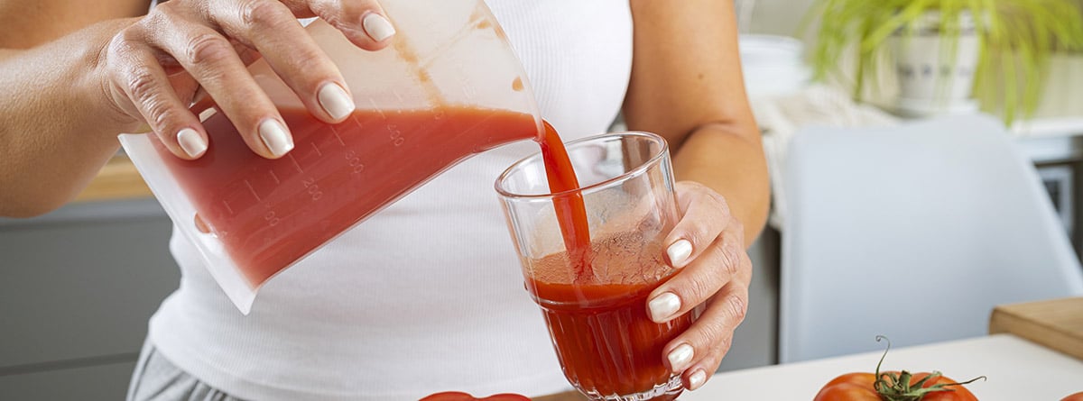 manos de mujer vertiendo jugo de tomate fresco en un vaso