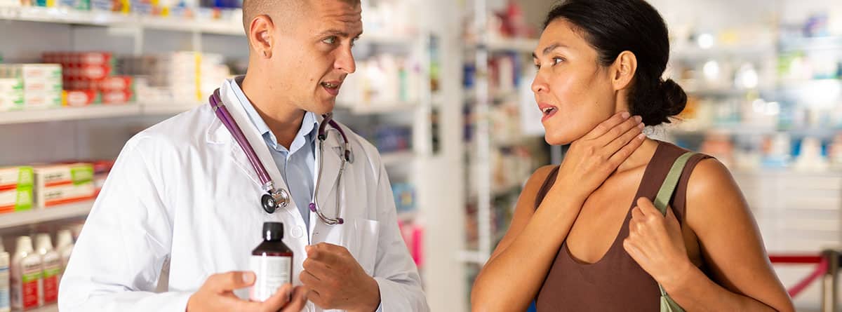 Farmacéutico enseñando un medicamento a una mujer con dolor de garganta