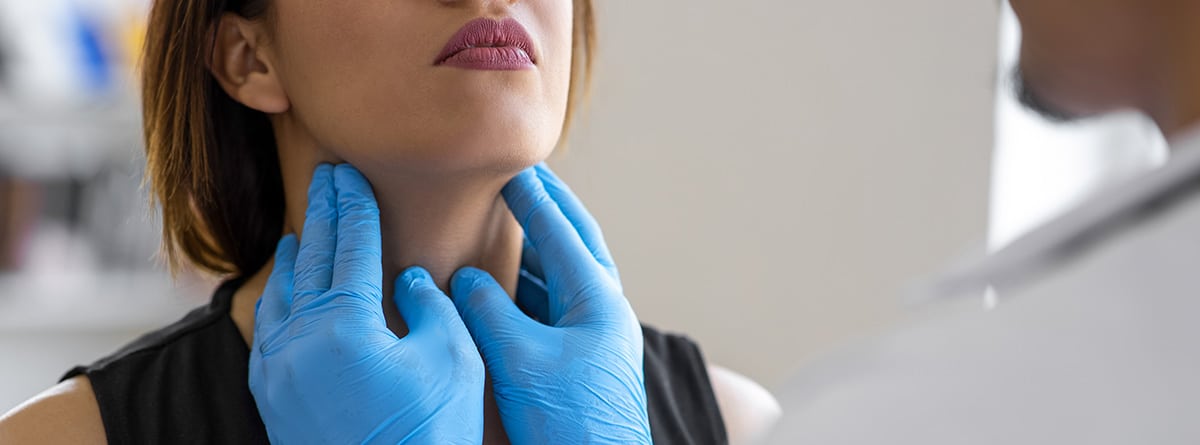 Manos con guantes de látex de color azul examinando la garganta a una mujer