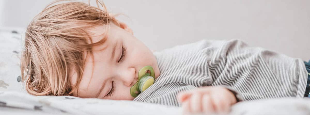 Bebé durmiendo con un chupete verde en la boca