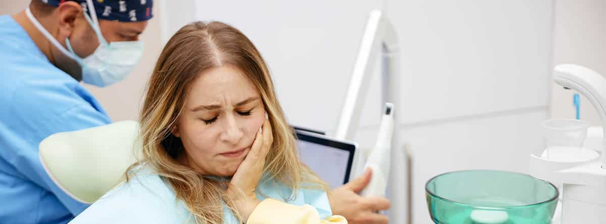 Mujer con la mano en la cara, con aspecto de tener dolor, en el dentista