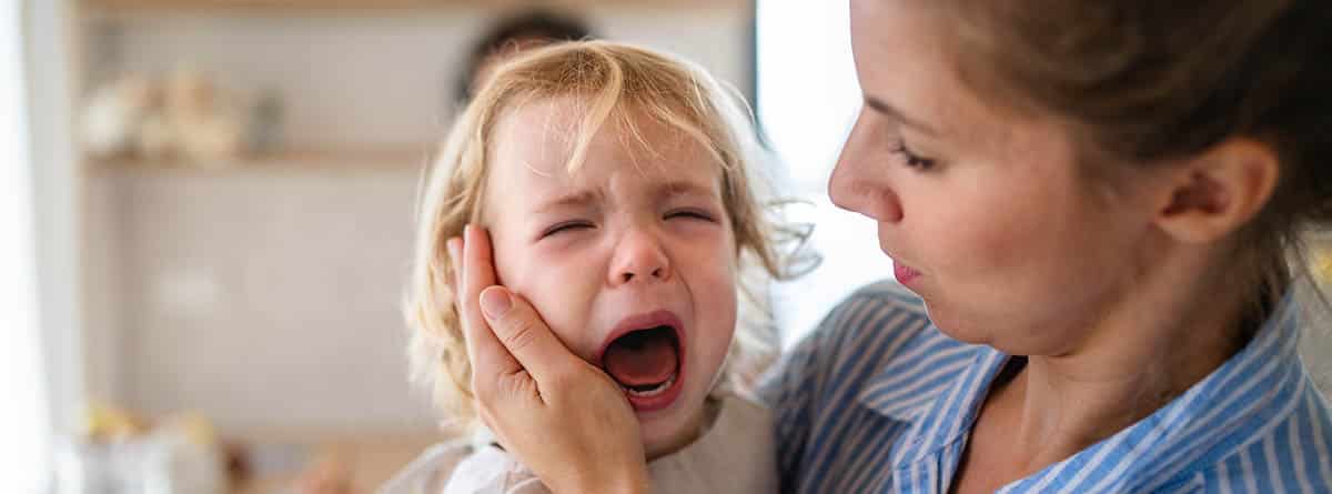 Niño de unos 2 años llorando en brazos de su madre, que trata de consolarle.