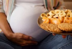 Tripa de embarazada con un plato con galletas y frutas