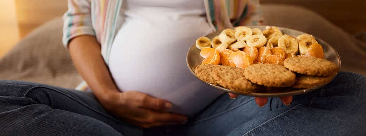 Tripa de embarazada con un plato con galletas y frutas