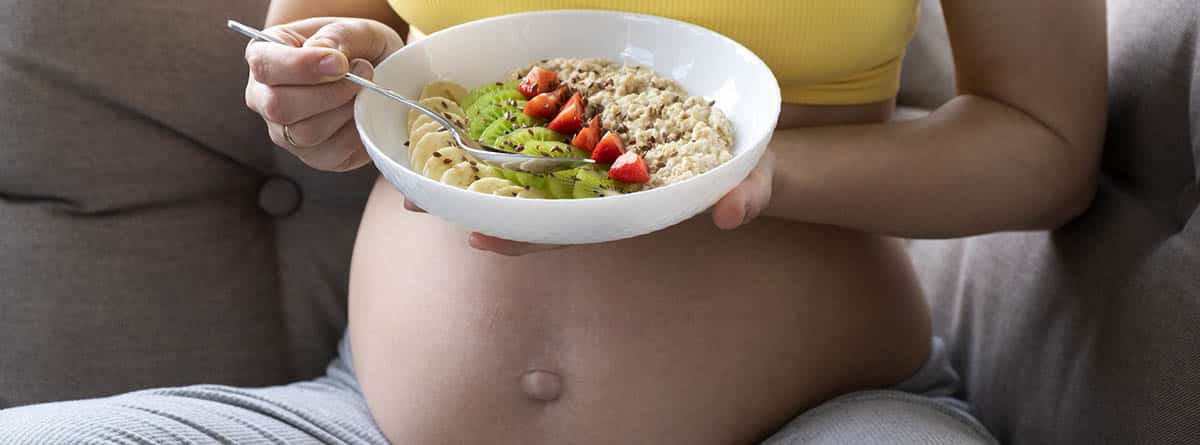 Tripa de embarazada con un plato con galletas y frutas